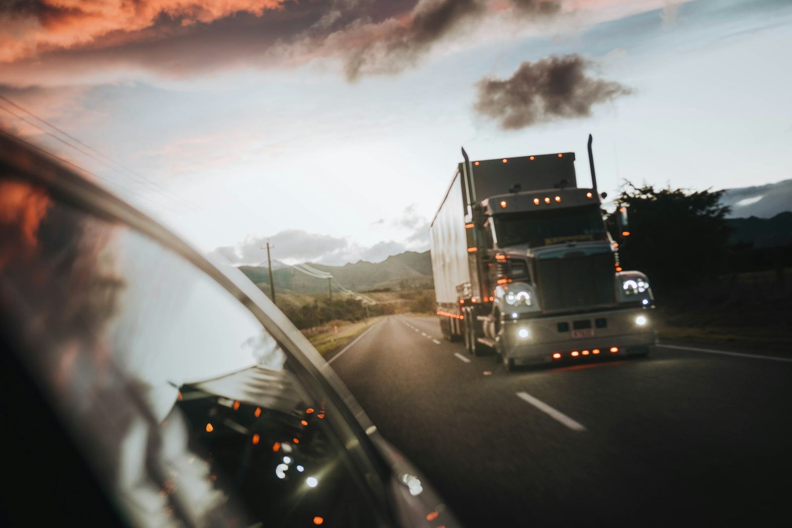 A truck on the road at dusk seen from a side mirror